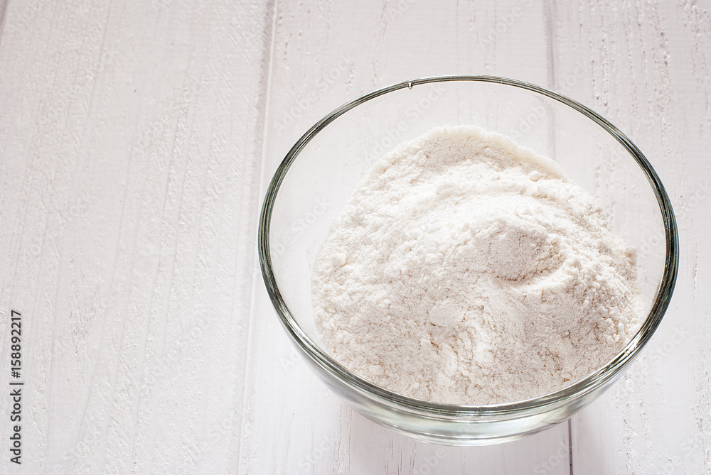 Flour in a transparent bowl on white boards Flour in a transparent bowl on white boards