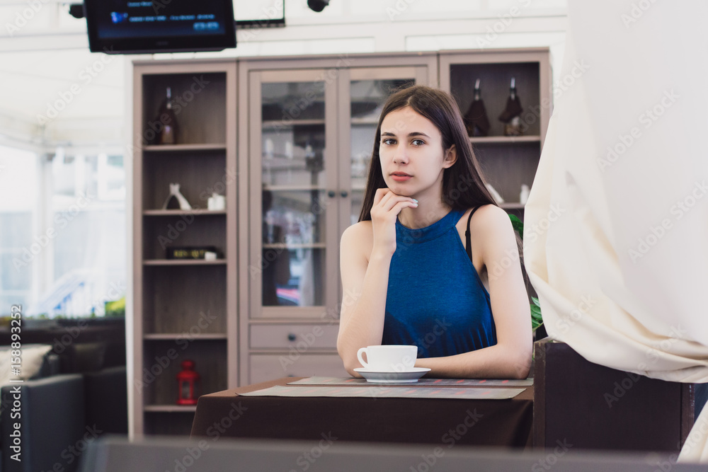 A very beautiful business woman sits in a cafe and holds a cup of coffee in her hands A very beautiful business woman sits in a cafe and holds a cup of coffee in her hands
