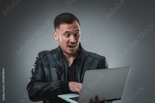 Man in black jacket looking at laptop, half turn. Holding opened laptop and working. Emotion. © nazarovsergey
