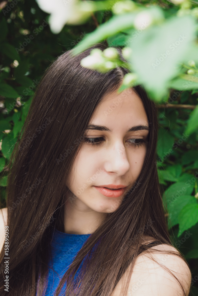 A very beautiful and cheerful girl stands on the street near a bush with white flowers A very beautiful and cheerful girl stands on the street near a bush with white flowers
