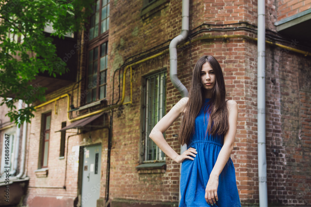 A very beautiful and cheerful girl stands on the street near a brick wall