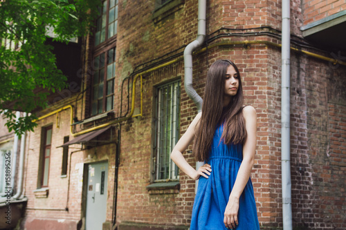 A very beautiful and cheerful girl stands on the street near a brick wall