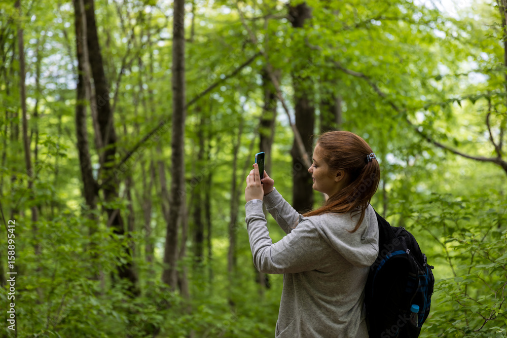 Young woman take a photo on her phone in the summer forest