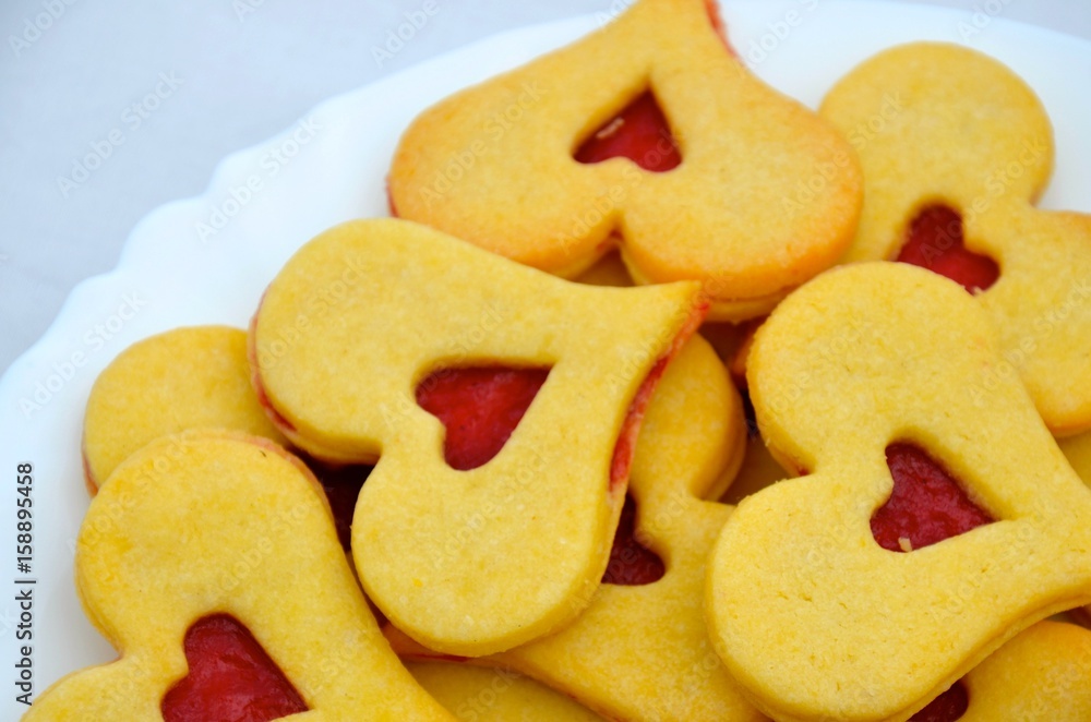 Traditional small Linz cakes in the shape of hearts. Filled by red berries jam. Detail photo of white plate. Valentine's, Christmas or wedding cookies. Traditional small Linz cakes in the shape of hearts. Filled by red berries jam. Detail photo of white plate. Valentine's, Christmas or wedding cookies.