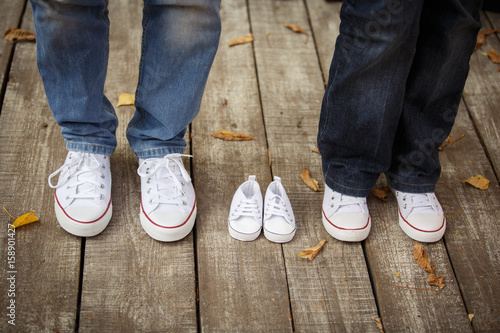 Waiting of baby. Little white baby's bootees near mom's and da's. Pregnant woman, pregnancy, motherhood. Happy family. Mom's, Dad's and baby's bootees. Family look photo