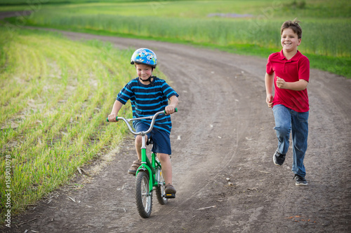 Fototapeta Naklejka Na Ścianę i Meble -  Two kids traveling together with his bike on rural landscape