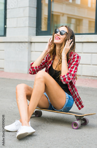 Beautiful young woman in sunglasses seat on skate, street fashion lifestyle.