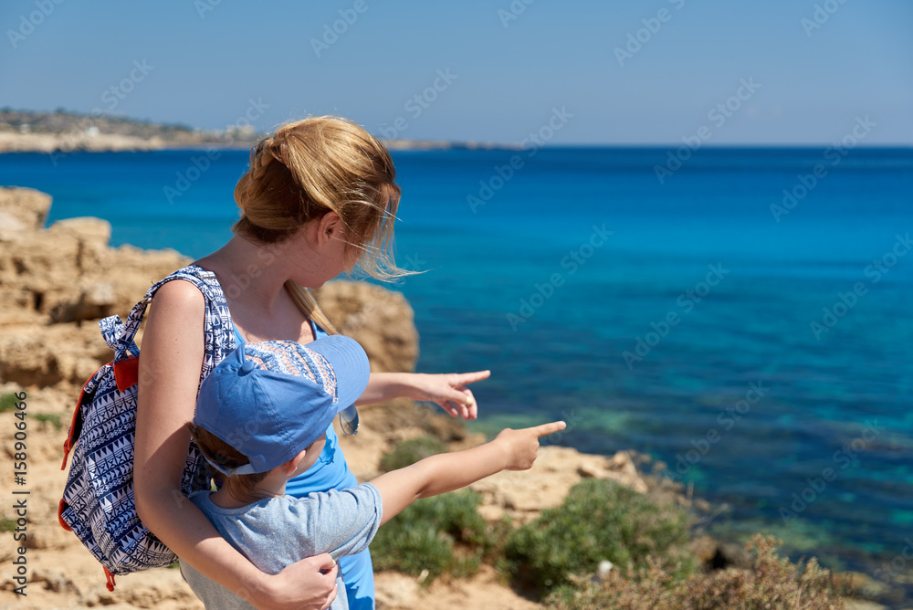 Mom and son spending time on the coast of the sea. They are pointing to something at the sea.