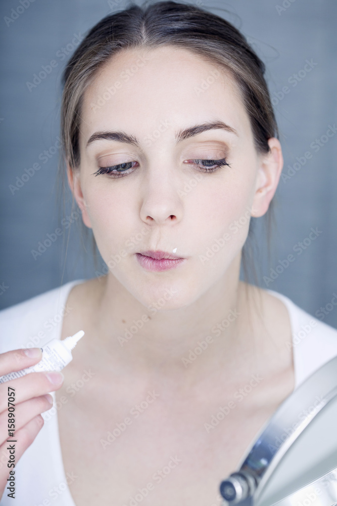 Woman applying cream to treat labial herpes Woman applying cream to treat labial herpes