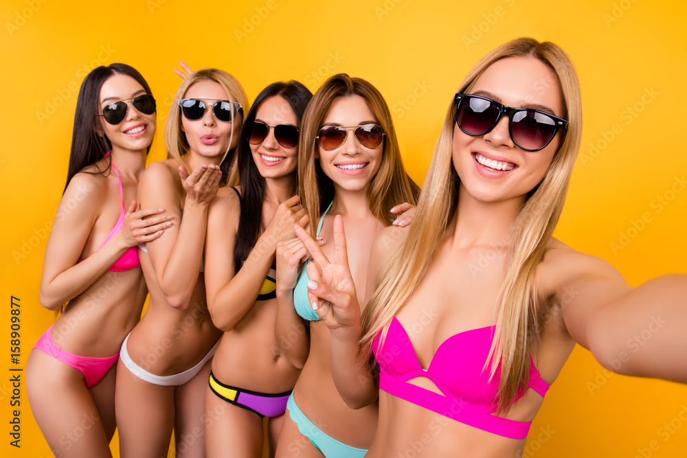 Cheers! Selfie mania! Joy time! Five young cute ladies in sunglasses are posing for a selfie photo shot, blond is taking. They are all in fashionable, trendy swim wear, gesturing, making memories
