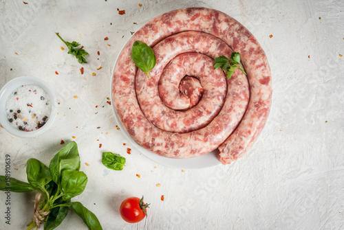 Raw homemade sausage from beef and pork. On a white table, with spices, herbs and tomatoes for cooking. Top view copy space