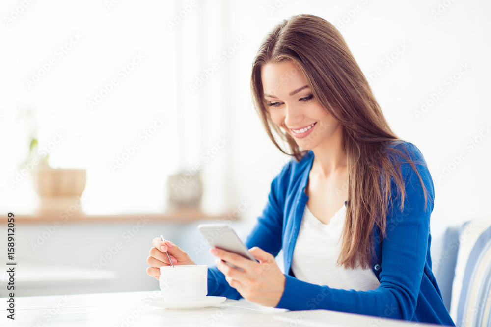 Young cute lady is browsing on her pda while having coffee in the cafe. She is in casual outfit, smiling, waiting for her friend Young cute lady is browsing on her pda while having coffee in the cafe. She is in casual outfit, smiling, waiting for her friend