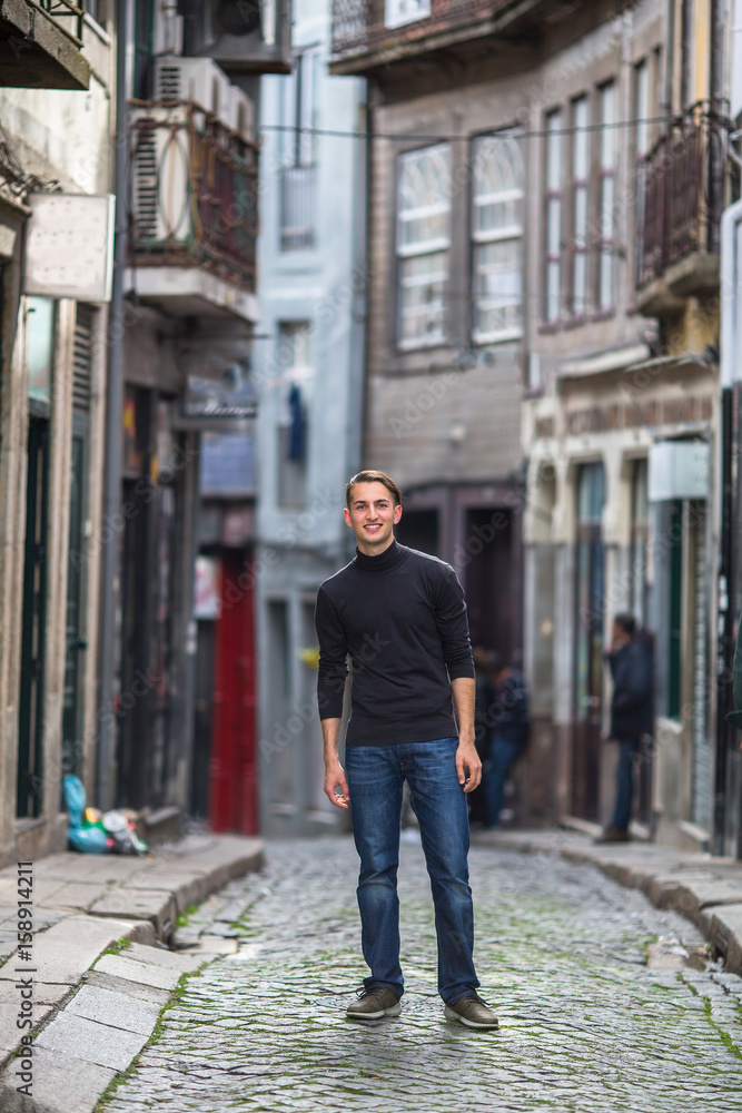 A young handsome guy is standing in a narrow street of the old town. A young handsome guy is standing in a narrow street of the old town.