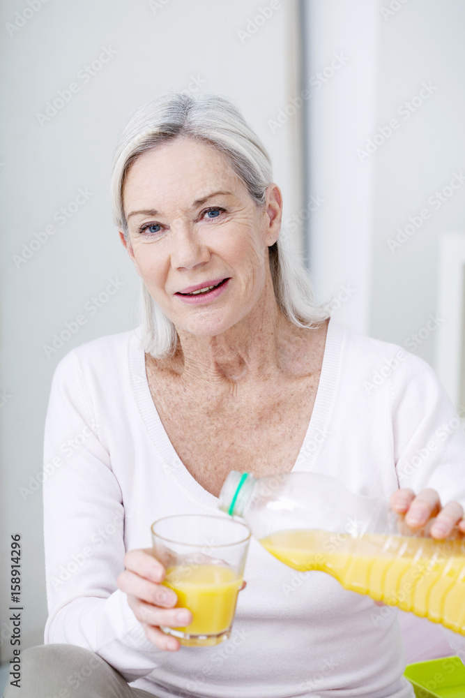 Senior woman pouring herself a glass of orange juice Senior woman pouring herself a glass of orange juice