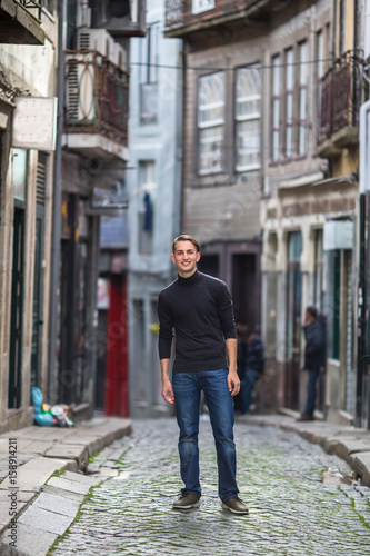 A young handsome guy is standing in a narrow street of the old town.