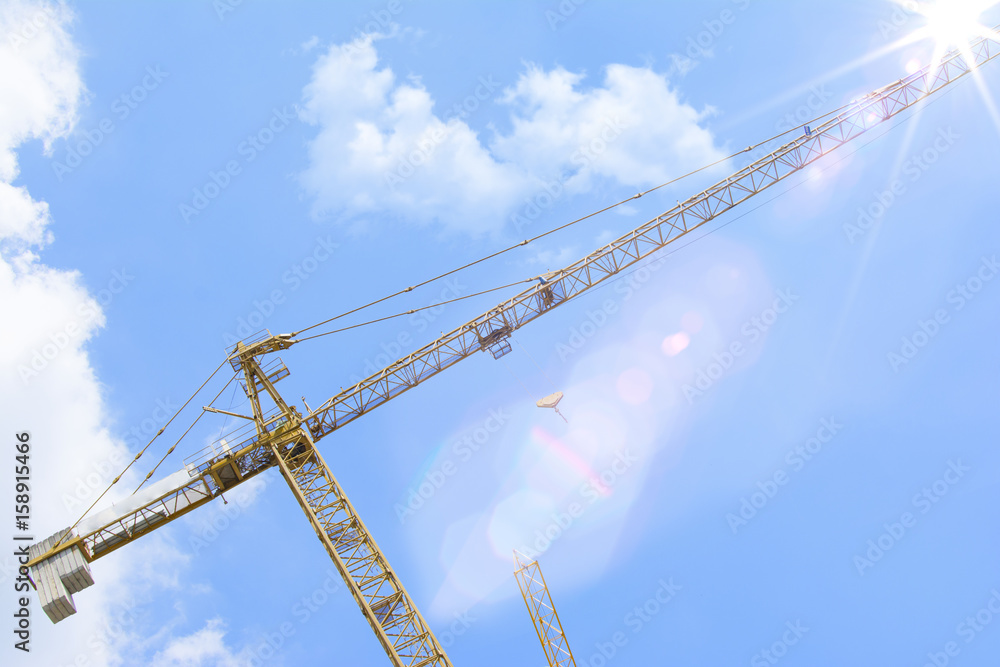 Industrial construction cranes over the beautiful blue sky. Lens flare in the background. Industrial construction cranes over the beautiful blue sky. Lens flare in the background.