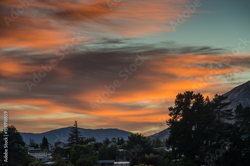 Queenstown  New Zealand - March 16  2017  Sunrise over the town paints parts of sky orange  offset by dark clouds  as if the horizon is on fire. Greenish sky breaks from the right which is the north.