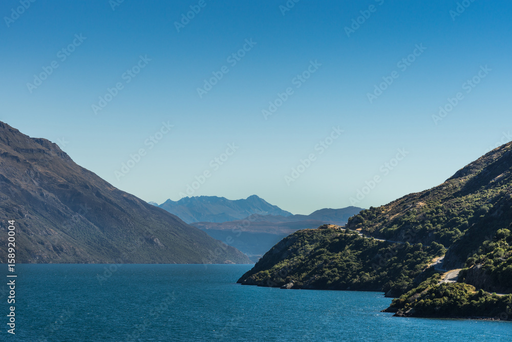 Queenstown, New Zealand - March 16, 2017: Looking south on northern arm of Lake Wakatipu near Eifin Bay. Blue water under full blue sky. Dark brown mountains and green vegetation on shores.