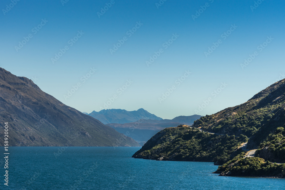 Queenstown, New Zealand - March 16, 2017: Looking south on northern arm of Lake Wakatipu near Eifin Bay. Blue water under full blue sky. Dark brown mountains and green vegetation on shores. Queenstown, New Zealand - March 16, 2017: Looking south on northern arm of Lake Wakatipu near Eifin Bay. Blue water under full blue sky. Dark brown mountains and green vegetation on shores.