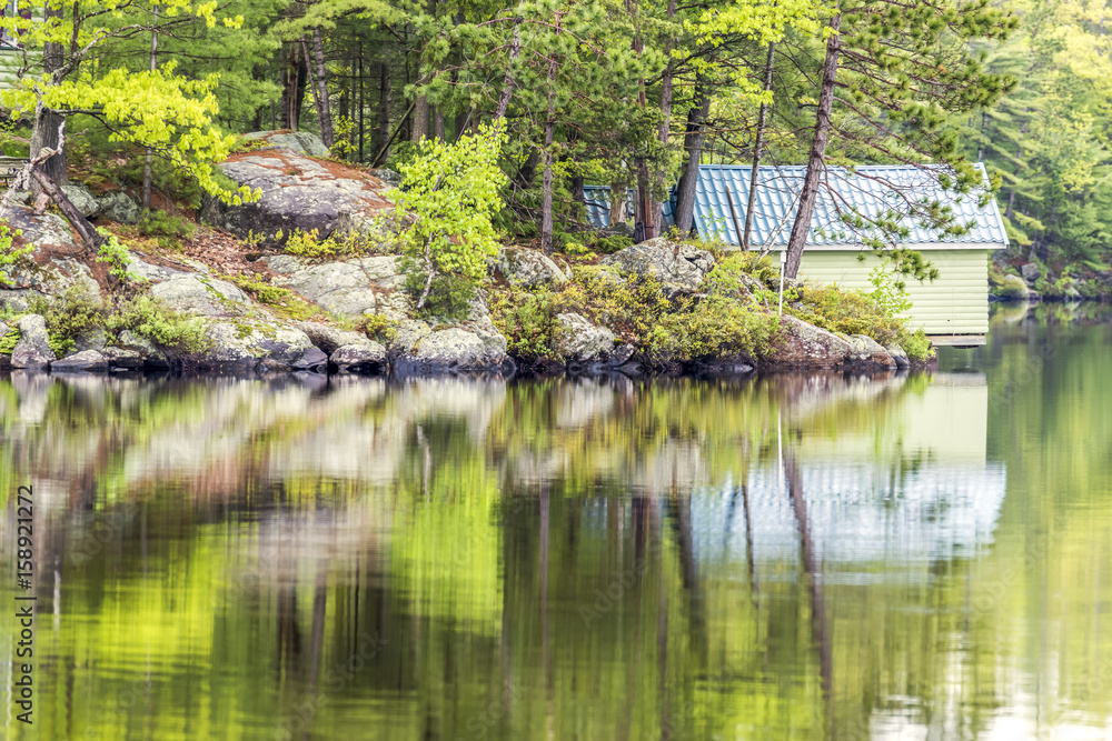 Rocks of Canadian shield and forest pine trees reflecting in water Rocks of Canadian shield and forest pine trees reflecting in water