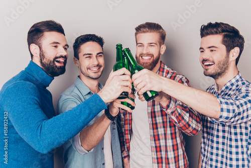 Close up portrait of four happy men friends, clinking their glasses of beer, smiling, alll are in casual outfits. They are fans of sports games as football, basketball, hockey, baseball photo