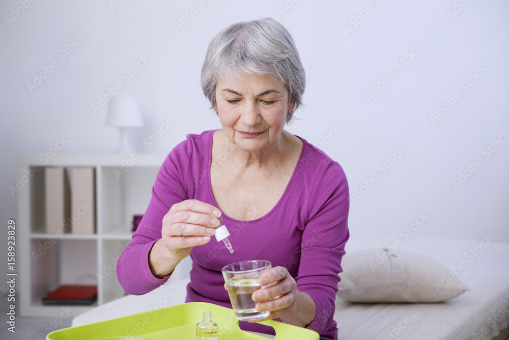 Senior woman pouring essential oil in a glass of water Senior woman pouring essential oil in a glass of water