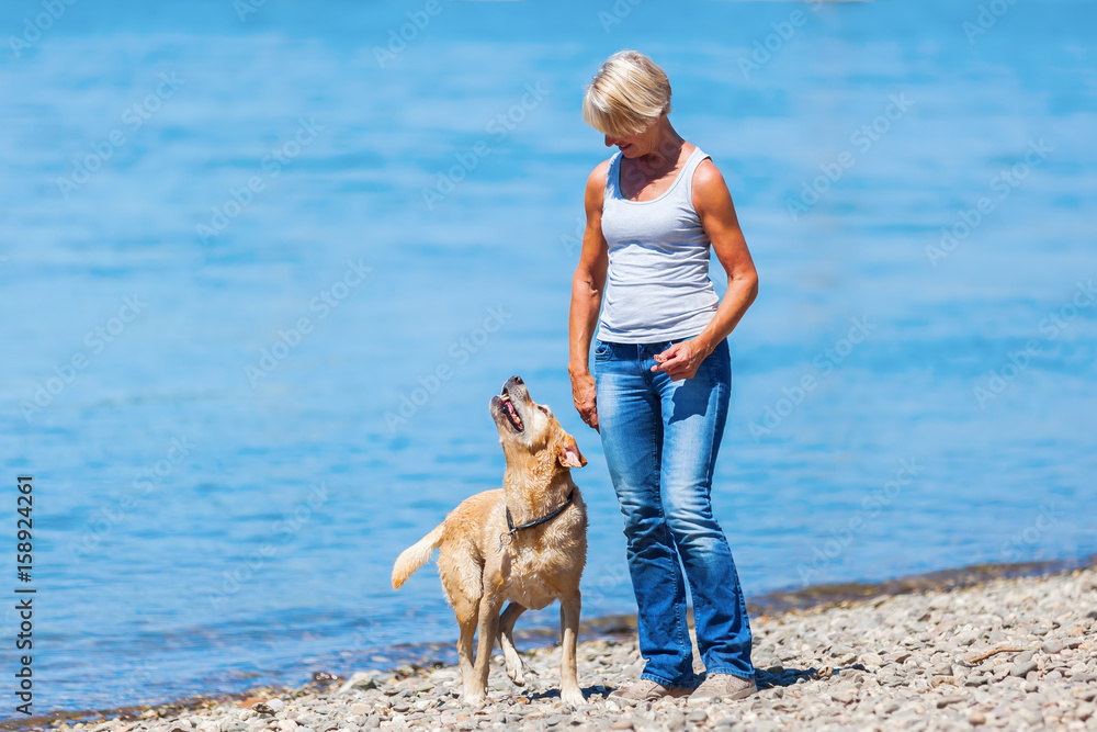 mature woman plays with a dog riverside