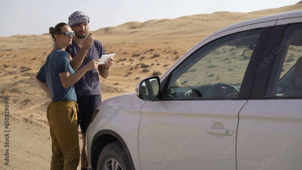Young couple with tablet checking map standing near car on dessert
Young couple with tablet checking map standing near car on dessert