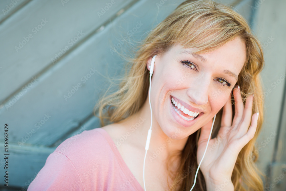 Fototapeta premium Outdoor Portrait of Young Adult Brown Eyed Woman Listening To Music with Earphones.