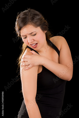 Beautiful young woman suffer from shoulder pain in a black background