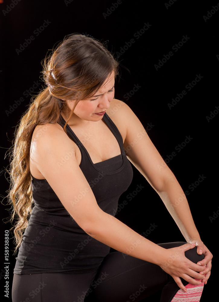 Beautiful young attractive sport woman holding injured knee suffering pain, in black background Beautiful young attractive sport woman holding injured knee suffering pain, in black background