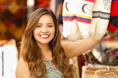 Close up of a beautiful woman holding an andean traditional handbag clothing textile yarn and woven by hand in wool, colorful fabrics background