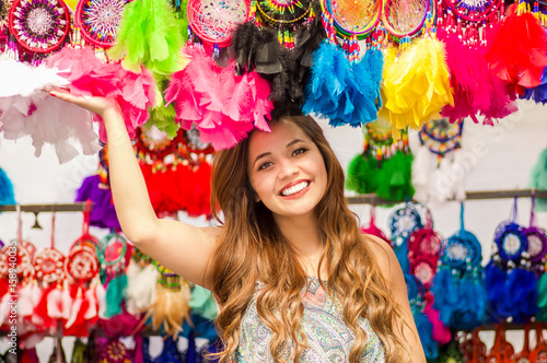 Beautiful smiling young woman touching a colorful catchdreamers, in colorful market fabrics background