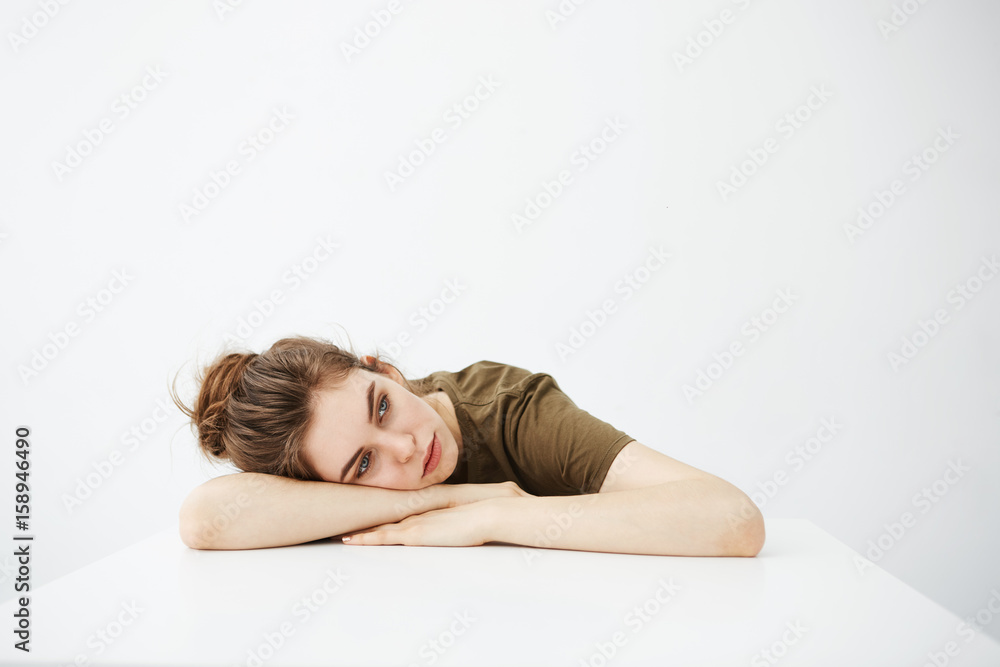Bored tired dull young girl student with bun sitting at table over white background. Bored tired dull young girl student with bun sitting at table over white background.