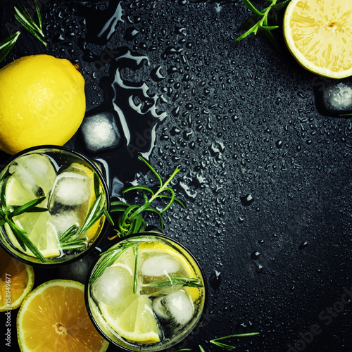 Summer cocktail with lemon, rosemary and ice, gray background, top view