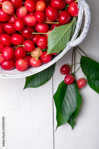 Red cherries in white basket on white wooden background. Cherry close up. Top view.