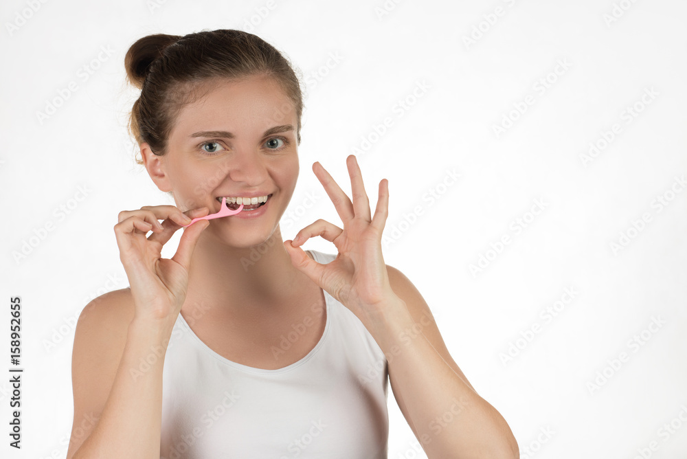 Hygiene of the oral cavity. Young girl cleans teeth with floss, smiling and showing okay sign on a background. Hygiene of the oral cavity. Young girl cleans teeth with floss, smiling and showing okay sign on a background.