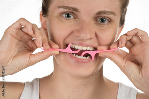 Hygiene of the oral cavity. Young girl cleans teeth with floss  smiling and showing okay sign on a background.