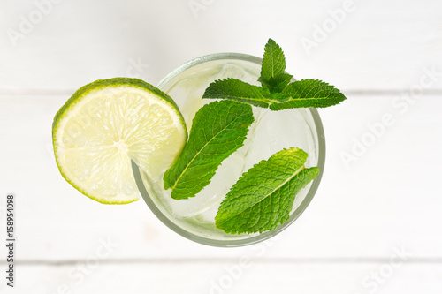 Mojito cocktail drink top view copy space in highball glass, summer tropical vacation beverage with rum, mint leaves, lime citrus juice, soda water and ice on white table background. Mock up.