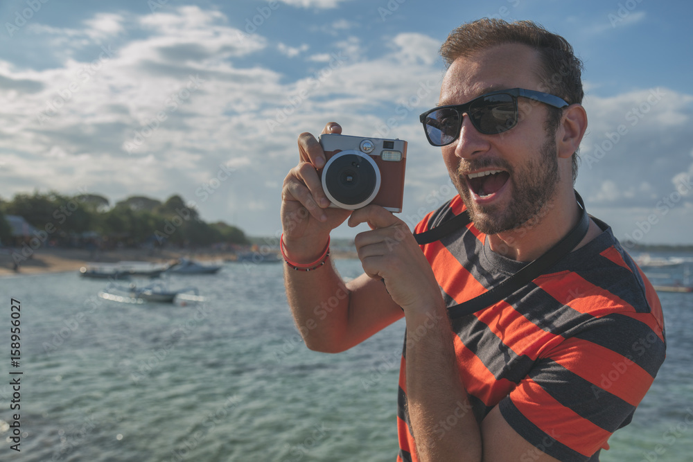 Obraz premium Man enjoying summer with his retro camera on the sea / ocean.