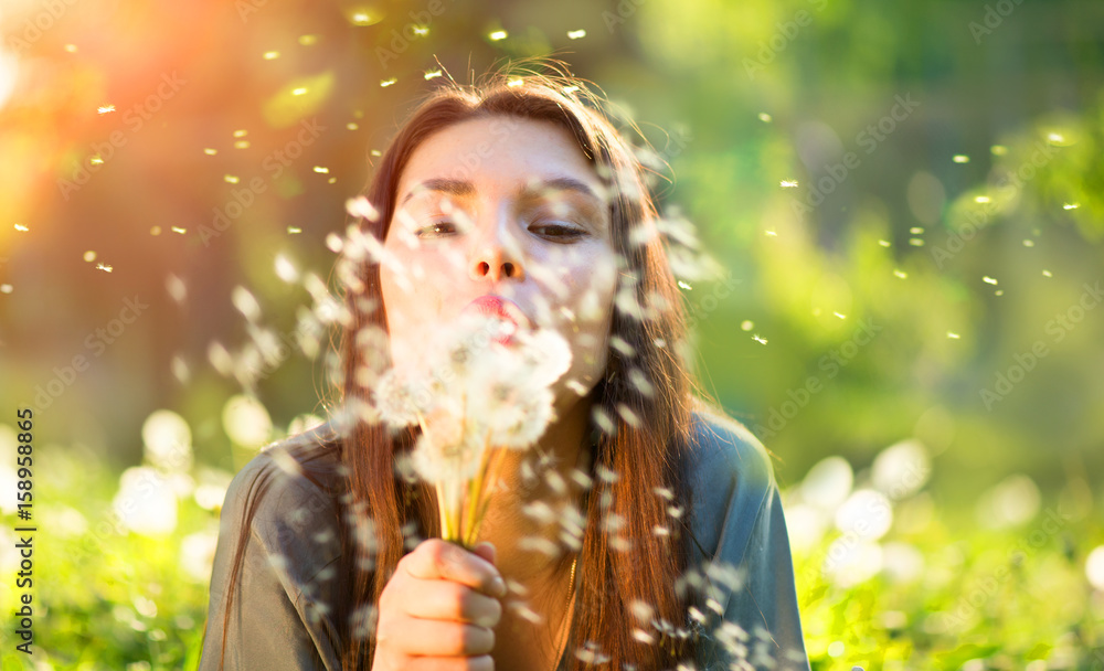 Obraz premium Piękna młoda kobieta leżąc na polu w zielonej trawie, dmuchanie mlecze i uśmiechnięte