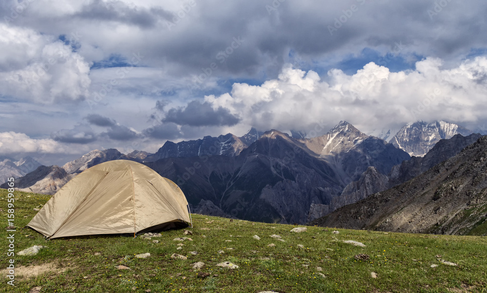 Tent standing on a mountain in the background of a high mountain pass, on the grass, sunny day, the beautiful sky with clouds.