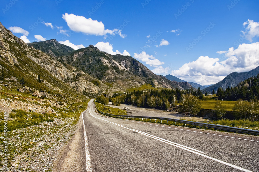 Chuiski road, Altai Republic. The road in the mountains, highway, paved road near the shore of the river Chuya. Sunny day in summer. Biking. Grass, herbs around.