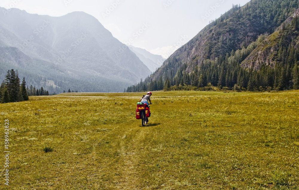 Biking in the Altai region. Russia, the Republic of Altai. Biking in Beluha area. A young woman, girl riding a bicycle. Sports hiking. Around the mountain, green, blue sky. Tourism.