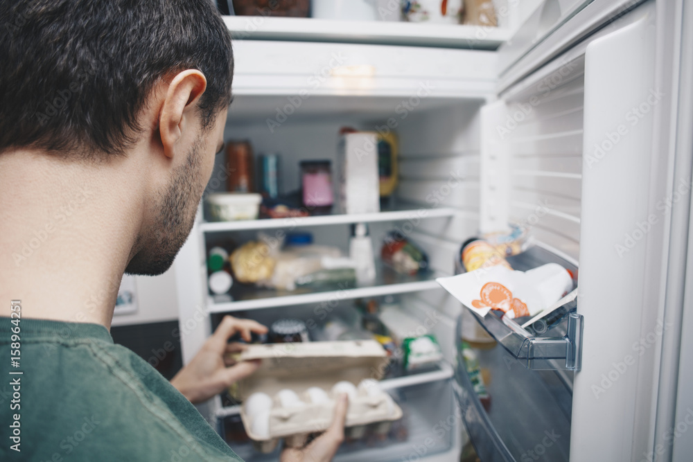 © Maskot - Man holding egg carton by refrigerator in kitchen