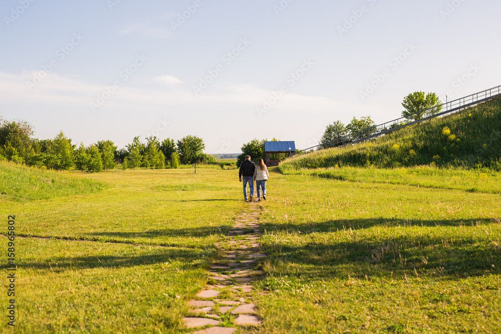 Man and woman holding hands and walking on country road, back view
