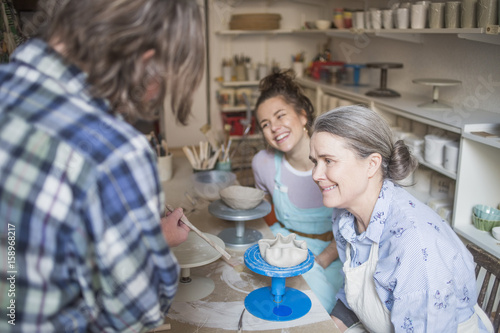 Happy female potters looking at mature colleague using hand tool at ceramic workshop photo