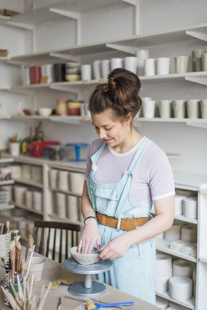 Smiling young potter molding shape on clay while standing by workbench at store Smiling young potter molding shape on clay while standing by workbench at store