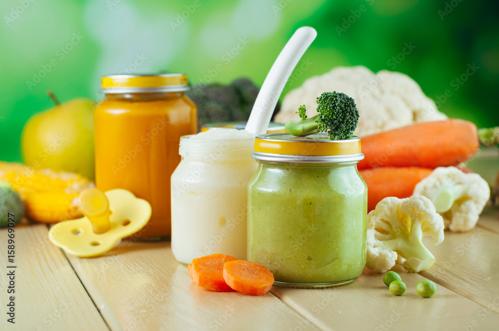 Jars with vegetable puree on the light wooden background Jars with vegetable puree on the light wooden background