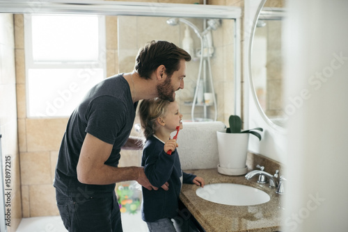 Side view of father watching daughter brushing teeth at sink in bathroom